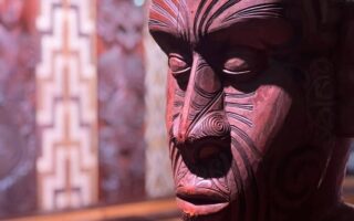 Nahaufnahme einer geschnitzten Māori-Figur mit markanten Gesichtsmotiven