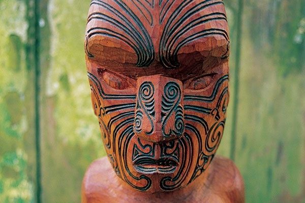 Nahaufnahme einer kunstvoll geschnitzten Māori-Figur mit Gesichtsornamenten